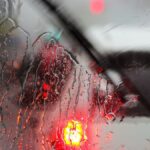 Raindrops on a car windshield with blurred traffic lights on rainy day.