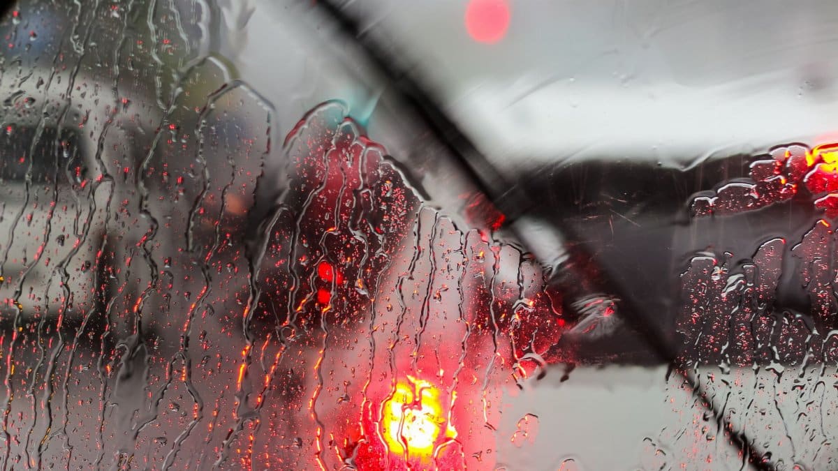 Raindrops on a car windshield with blurred traffic lights on rainy day.