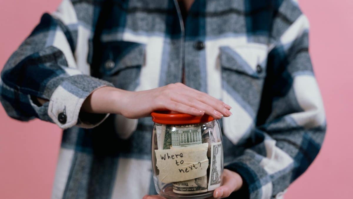 Woman in plaid shirt holds money jar with travel goals in mind.