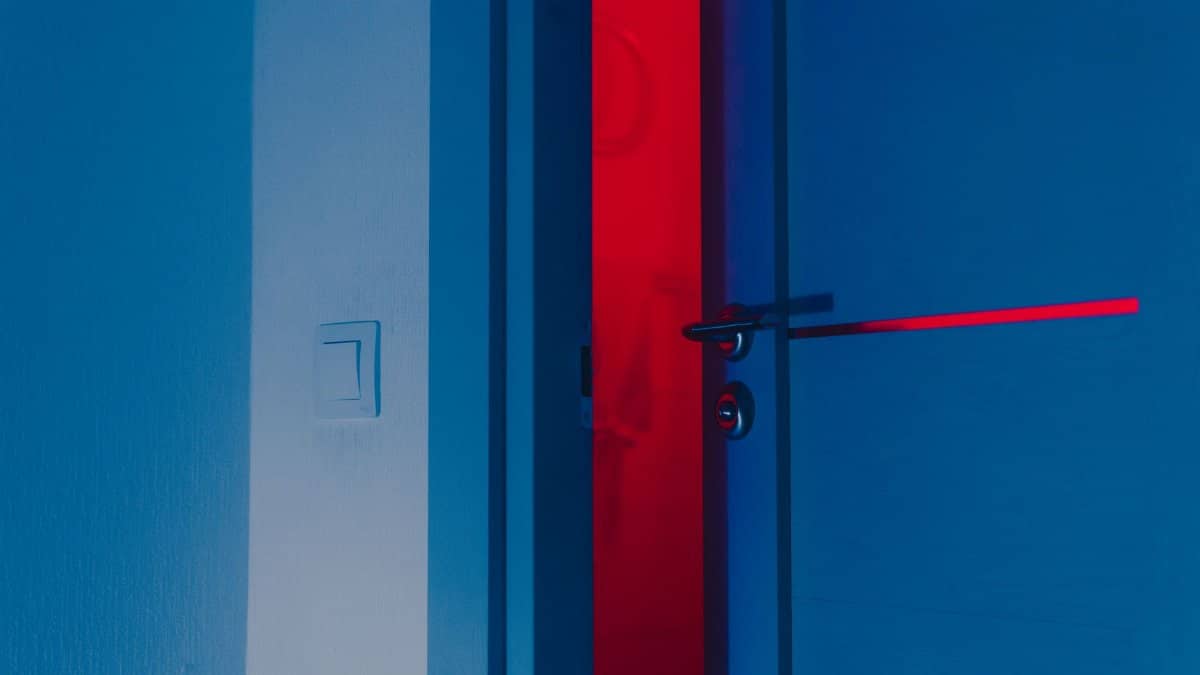 A half-open blue door illuminated by a dramatic red light reveals a unique interior atmosphere.