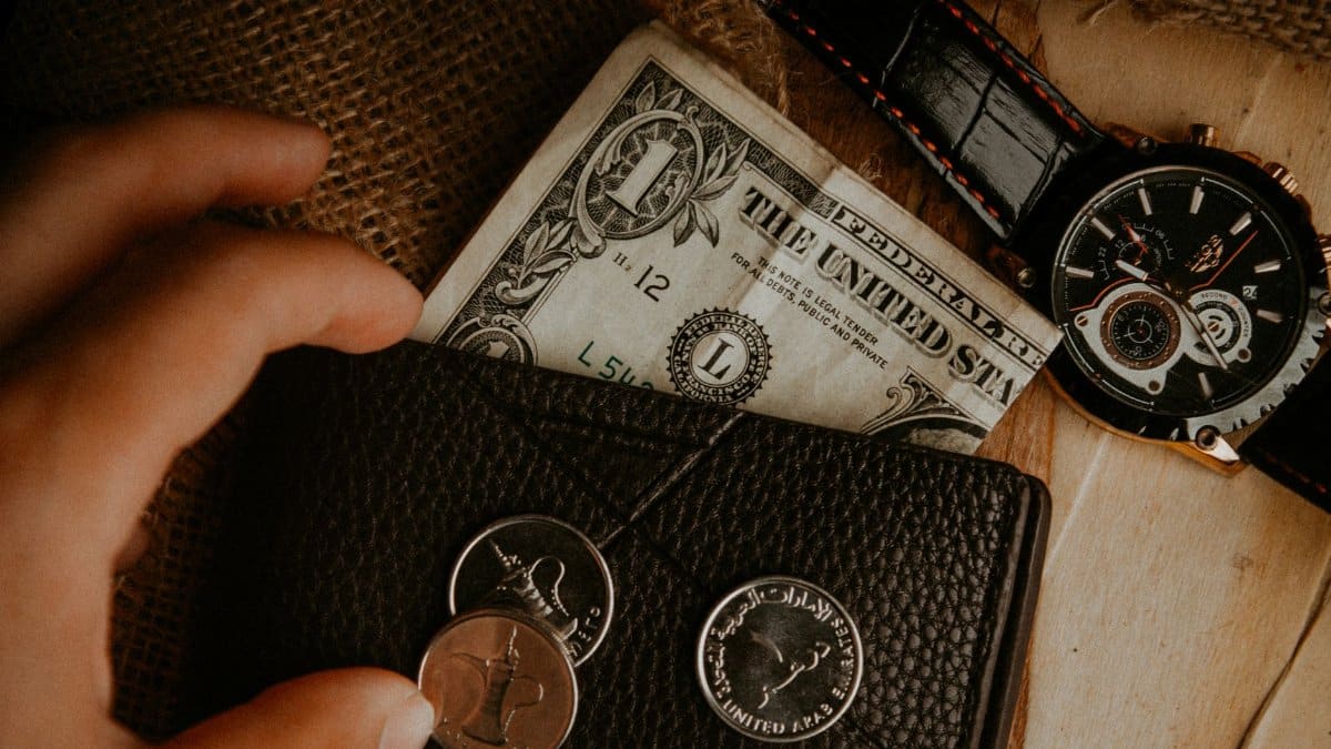 A detailed look at a wallet with money and a watch on a wooden surface.