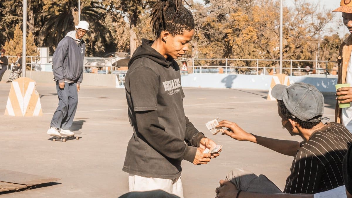 Group of young men exchanging money at a sunny outdoor skate park.