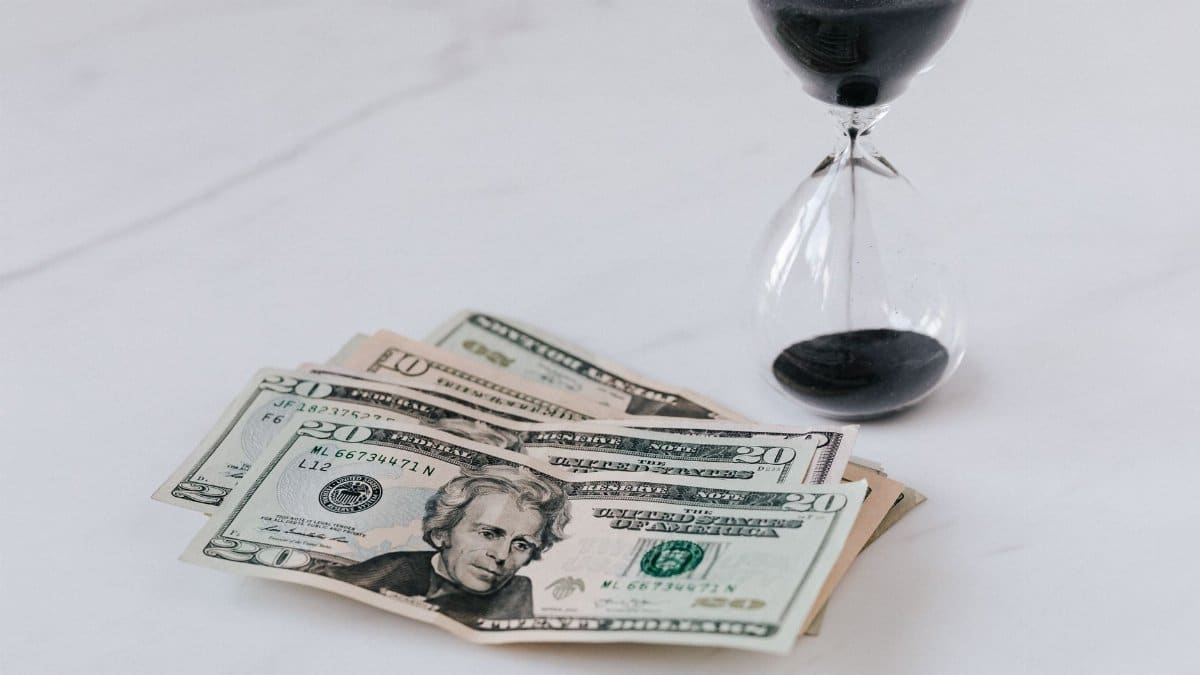 From above of transparent glass with black sand on white table and pile of paper money with image of president