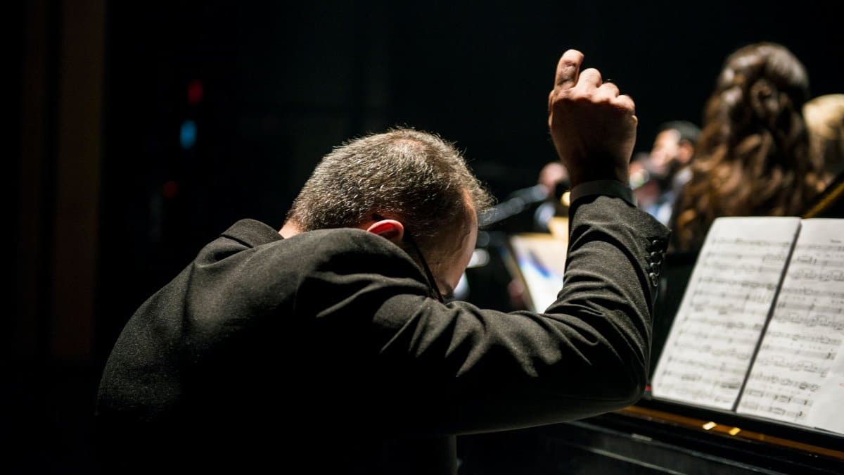 A conductor passionately leads an orchestra during a live performance with visible sheet music.