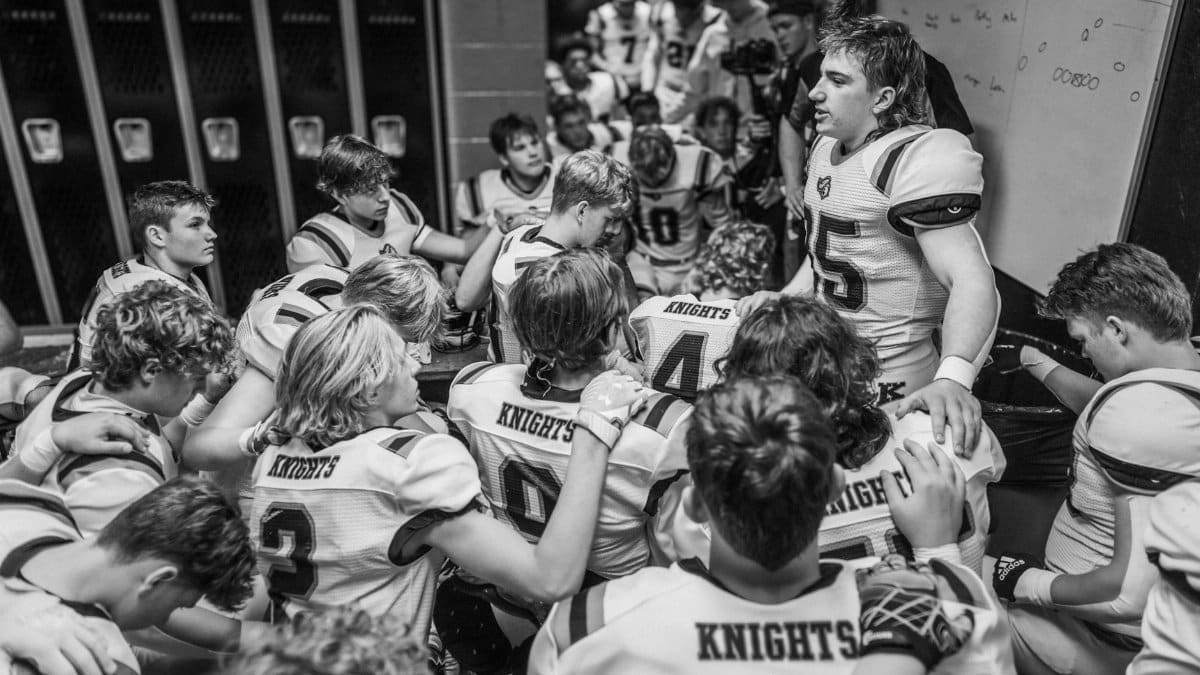 High school football team huddles in locker room for motivational talk before game.