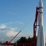 Vostok rocket stands poised on launch pad under clear blue sky at space center.