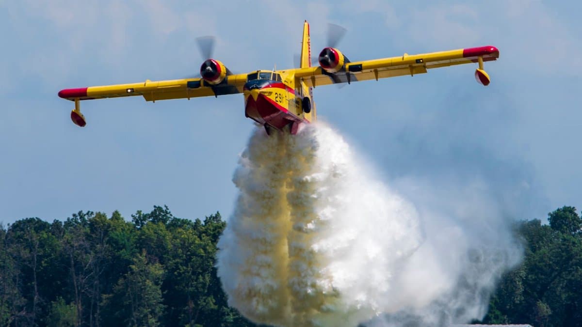 A firefighting aircraft releasing water to combat a forest fire in daylight.