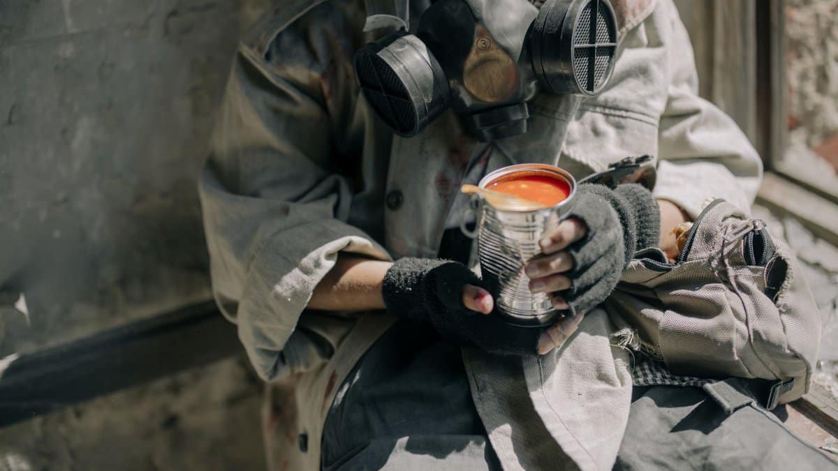 A person wearing a gas mask holding canned tomato soup, symbolizing survival.