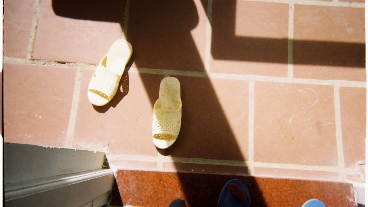 Two slippers on terracotta tiles casting shadows in bright sunlight.