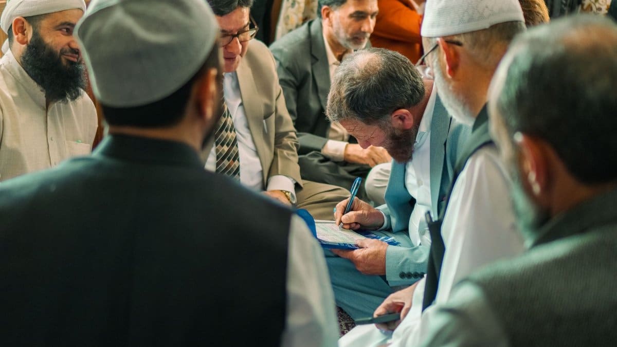 Men in traditional and modern attire engaged in a formal discussion indoors.