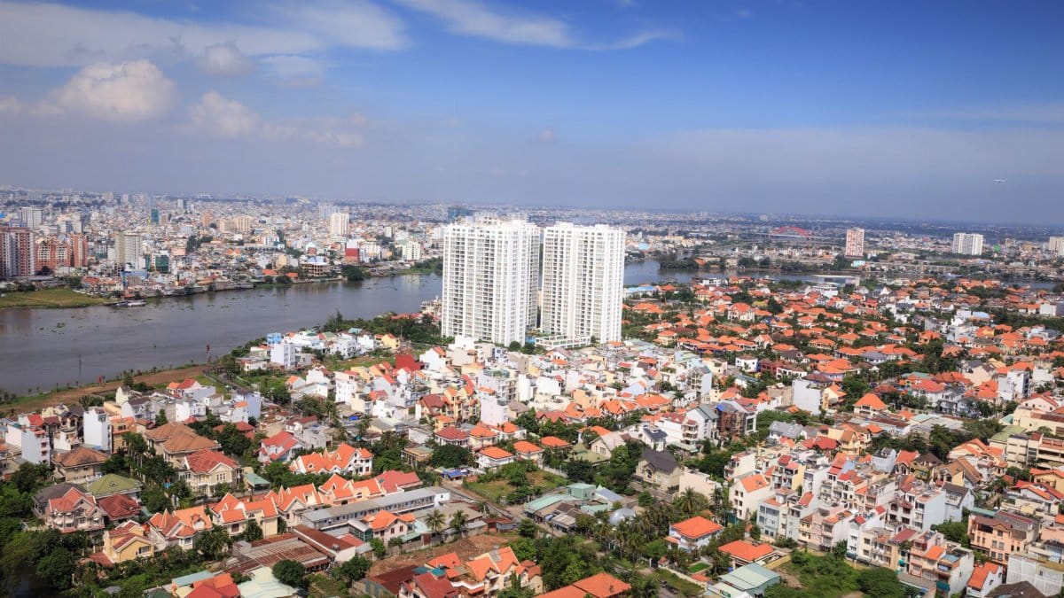 Aerial view of Ho Chi Minh City's urban landscape along a river, showcasing high-rise buildings and vibrant neighborhoods.