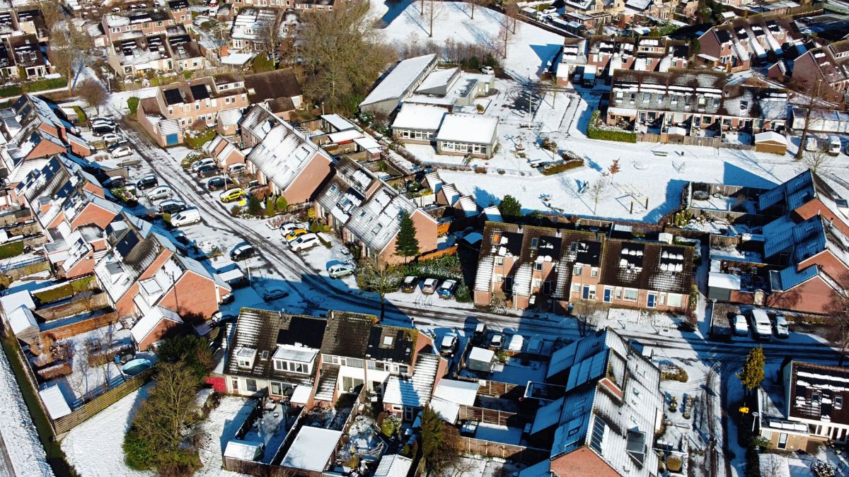 Aerial view of snow-covered houses in a suburban residential district under bright sunlight.