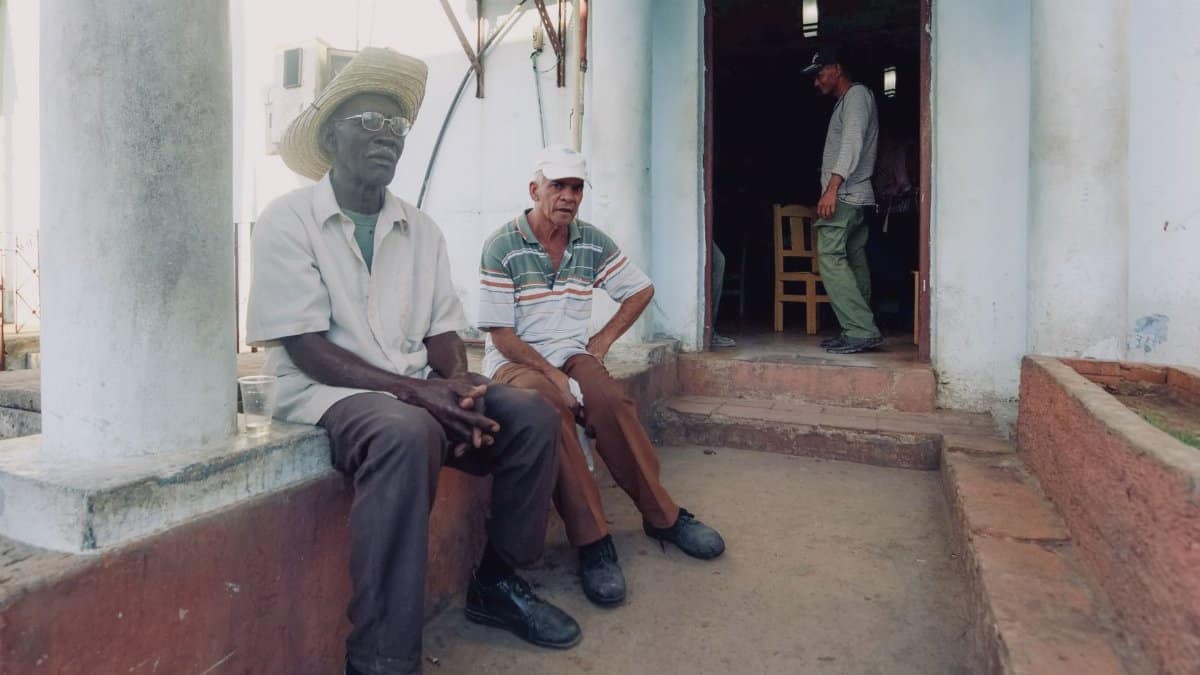 Three men seated and standing by a doorway of a house, engaging in conversation.
