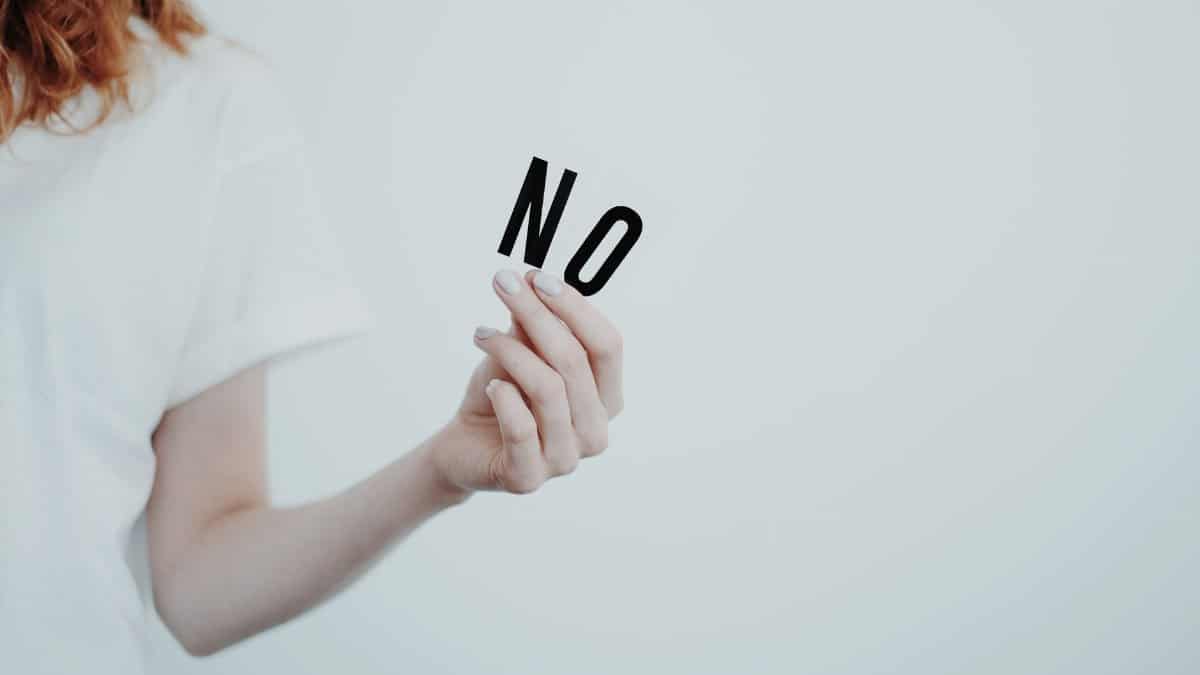 Close-up of person holding the word 'NO' in black letters on a white background, conveying a message of refusal.