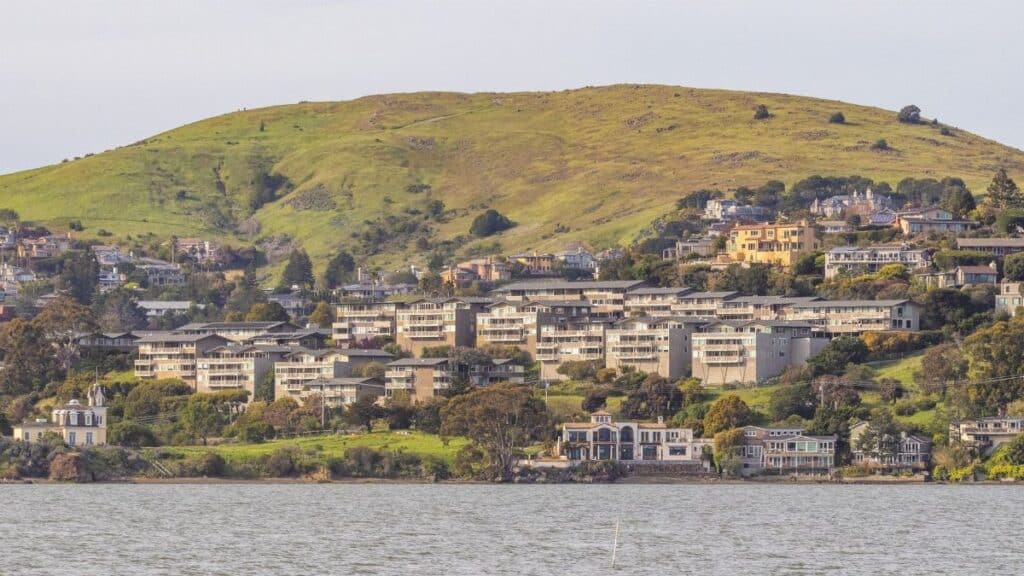 Picturesque hillside town with waterfront view, featuring lush green hills and residential buildings.