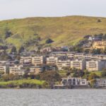 Picturesque hillside town with waterfront view, featuring lush green hills and residential buildings.