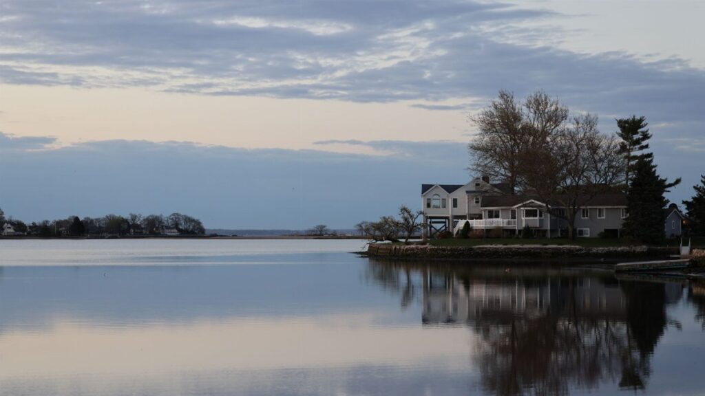 Peaceful twilight scene of lakeside houses reflecting on calm water in Stamford, Connecticut.