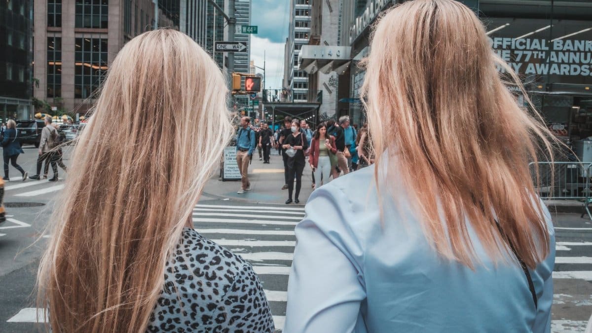 Two women with long hair stand on a busy crosswalk in New York City, USA.