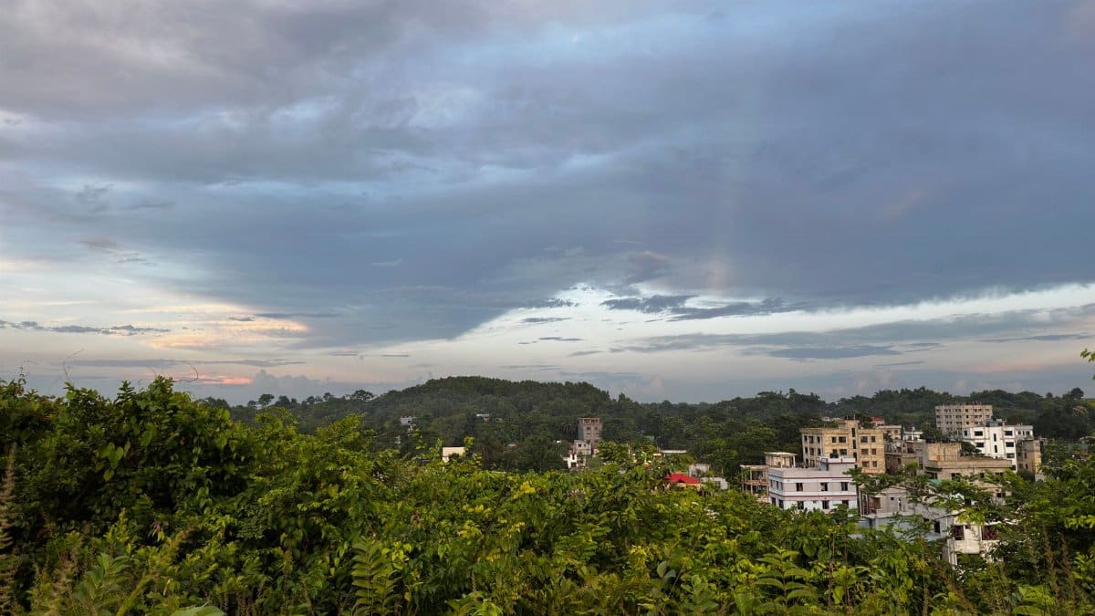 A picturesque view of a small urban area surrounded by lush greenery under a cloudy sky.