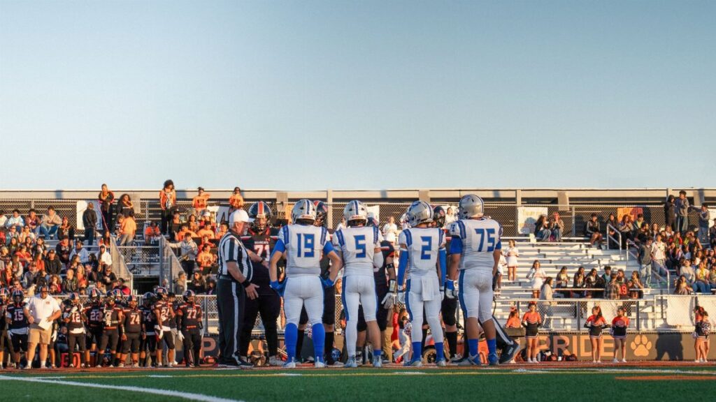 A high school football game during sunset with players and a referee on the field.