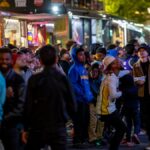 A lively crowd gathers around vibrant food trucks at night, enjoying a bustling street food experience.