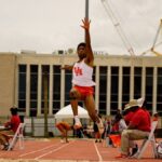 Dynamic shot of an athlete performing a mid-air long jump at a track event in Houston, Texas.