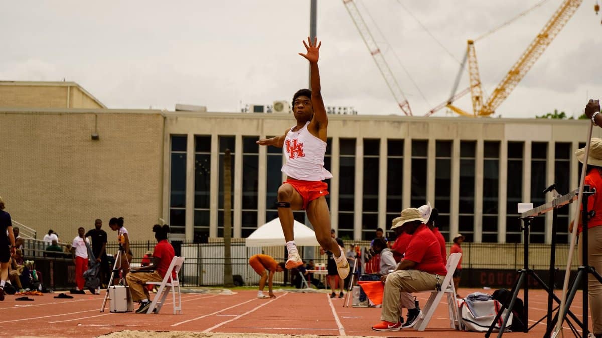 Dynamic shot of an athlete performing a mid-air long jump at a track event in Houston, Texas.