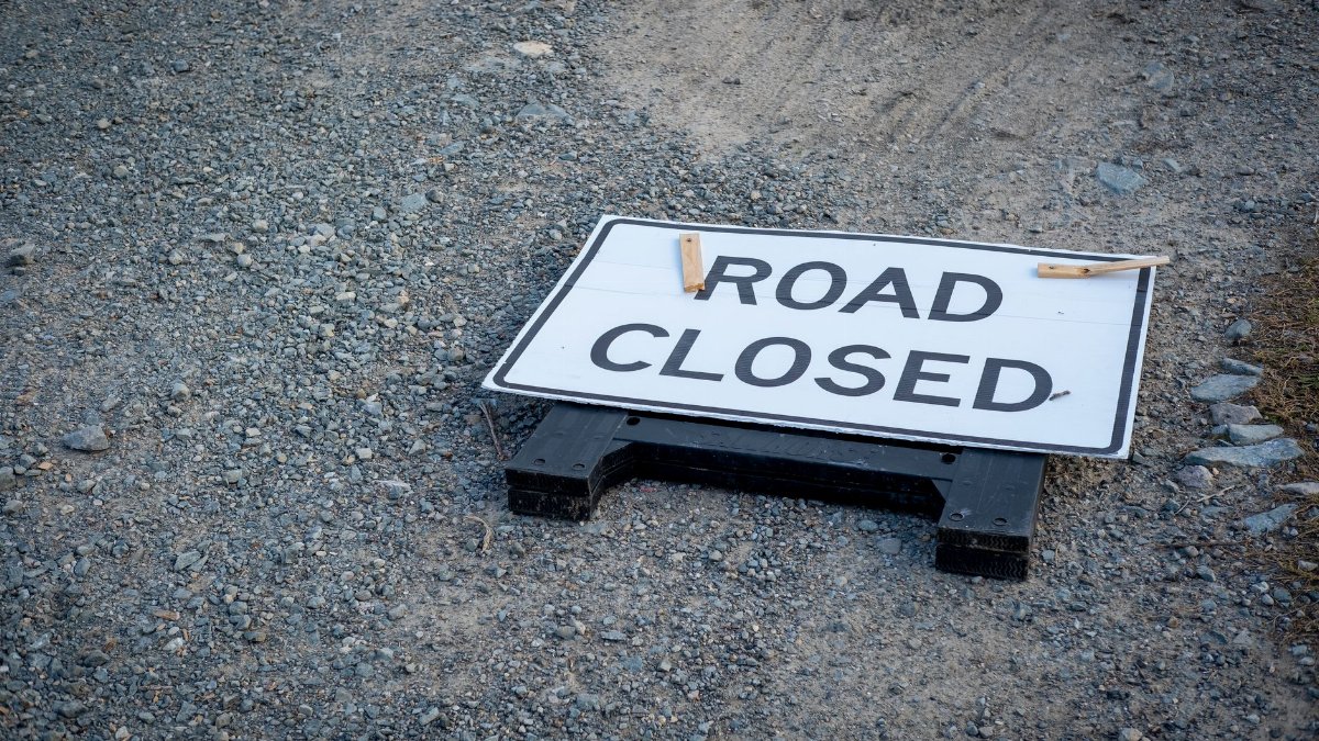 A road closed sign lies on a gravel pathway, indicating a blocked road ahead.
