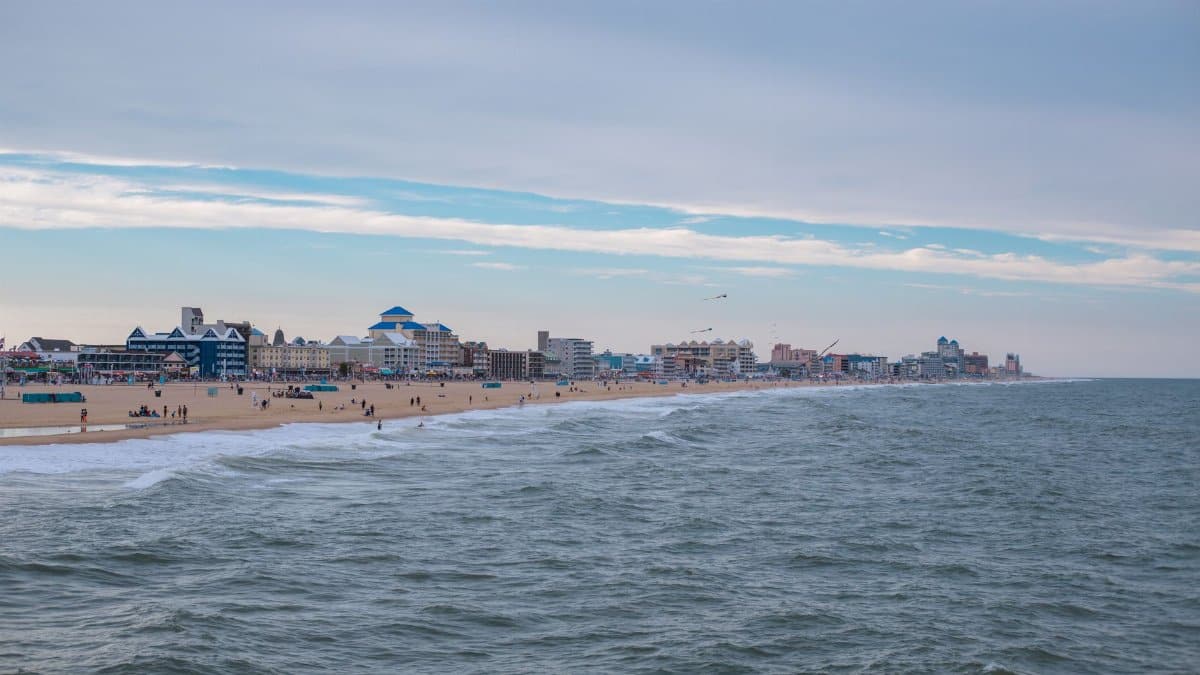 Peaceful beach scene with city buildings and a vast ocean under a serene sky.
