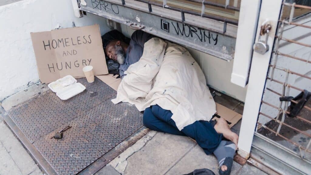 A homeless man sleeps on the street illustrating hardship and poverty.