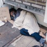 A homeless man sleeps on the street illustrating hardship and poverty.