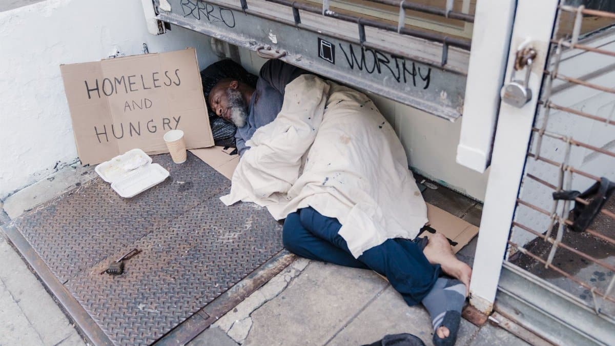 A homeless man sleeps on the street illustrating hardship and poverty.