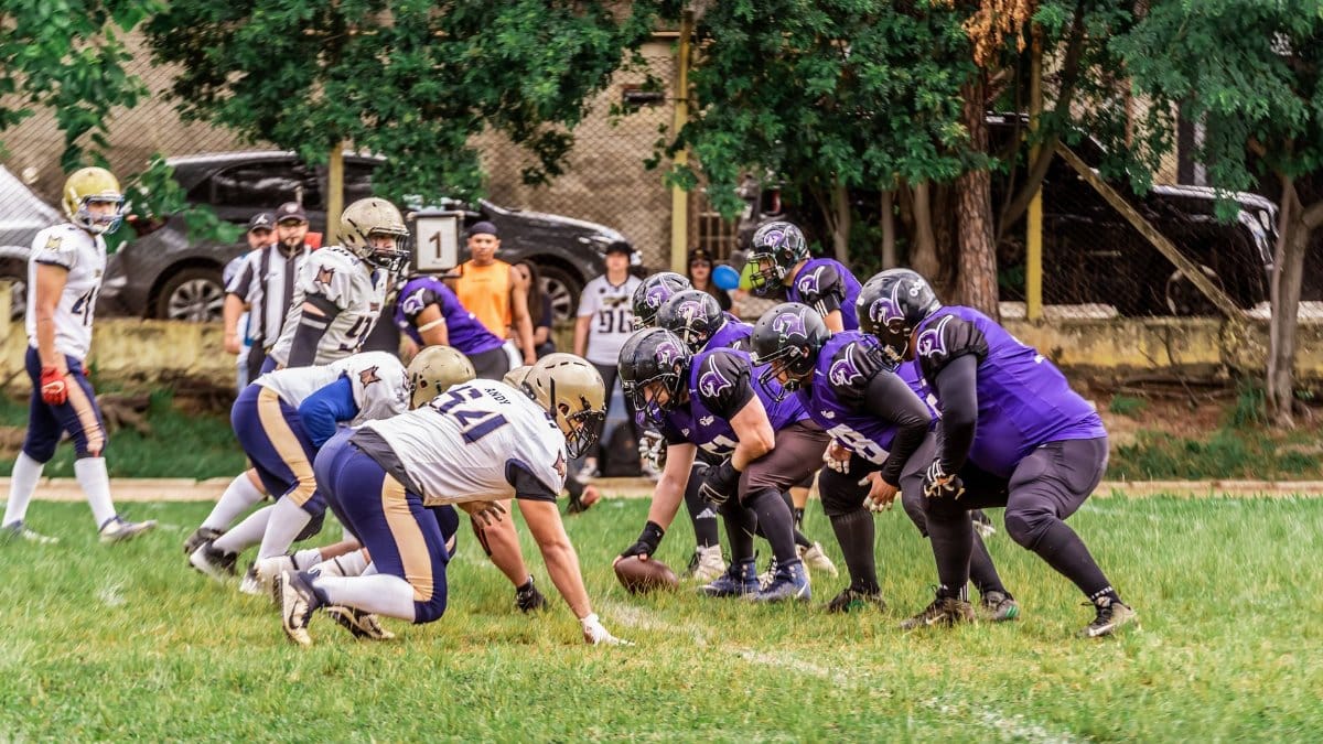 Two American football teams face off during a lively game on a grassy field.