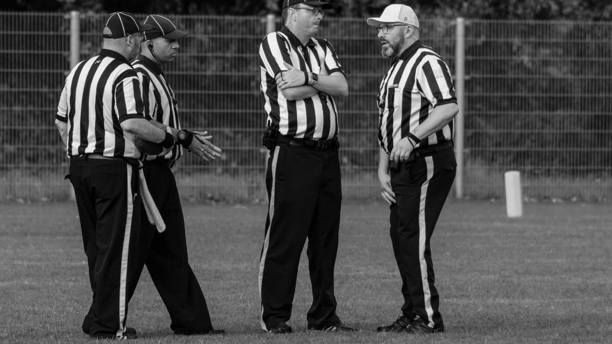 Four referees in striped uniforms discuss on a grassy field.