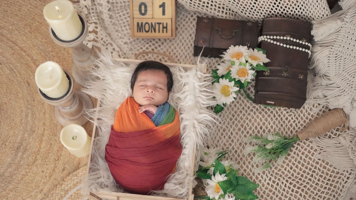 Adorable one-month-old baby wrapped in rainbow swaddle with flowers and candles, celebrating first month milestone.
