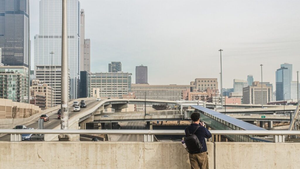 A man photographs the urban cityscape and highway of downtown Chicago, capturing skyscrapers and modern architecture.