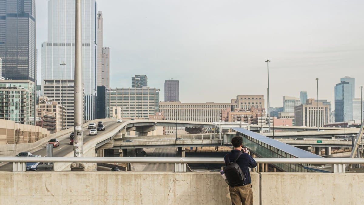 A man photographs the urban cityscape and highway of downtown Chicago, capturing skyscrapers and modern architecture.