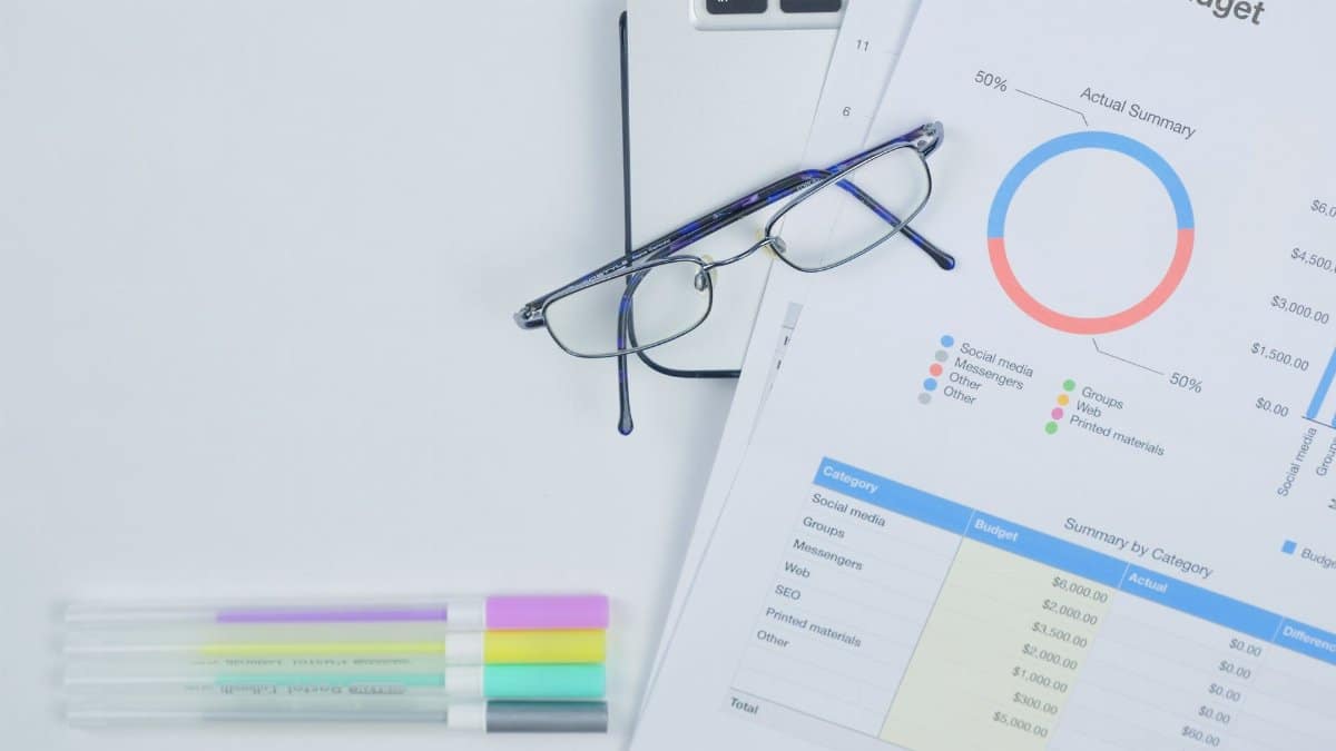 A modern workspace featuring budget graph, laptop, glasses, and stationery for creative business planning.