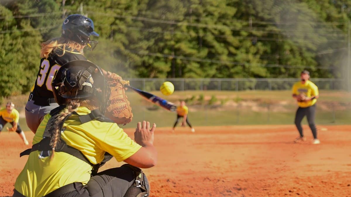 Dynamic action shot of a high school softball game capturing the batter, catcher, and field players.