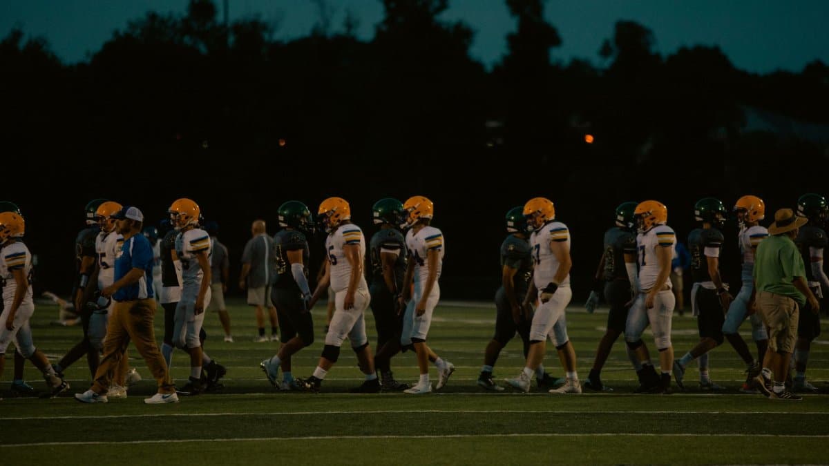 Teams shake hands post-game on a football field under the night sky.