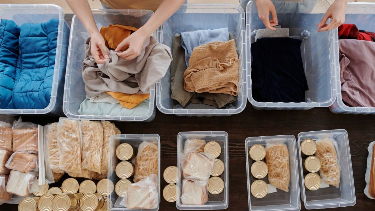 Volunteers organize donated clothes and food cans in clear containers for charity support.
