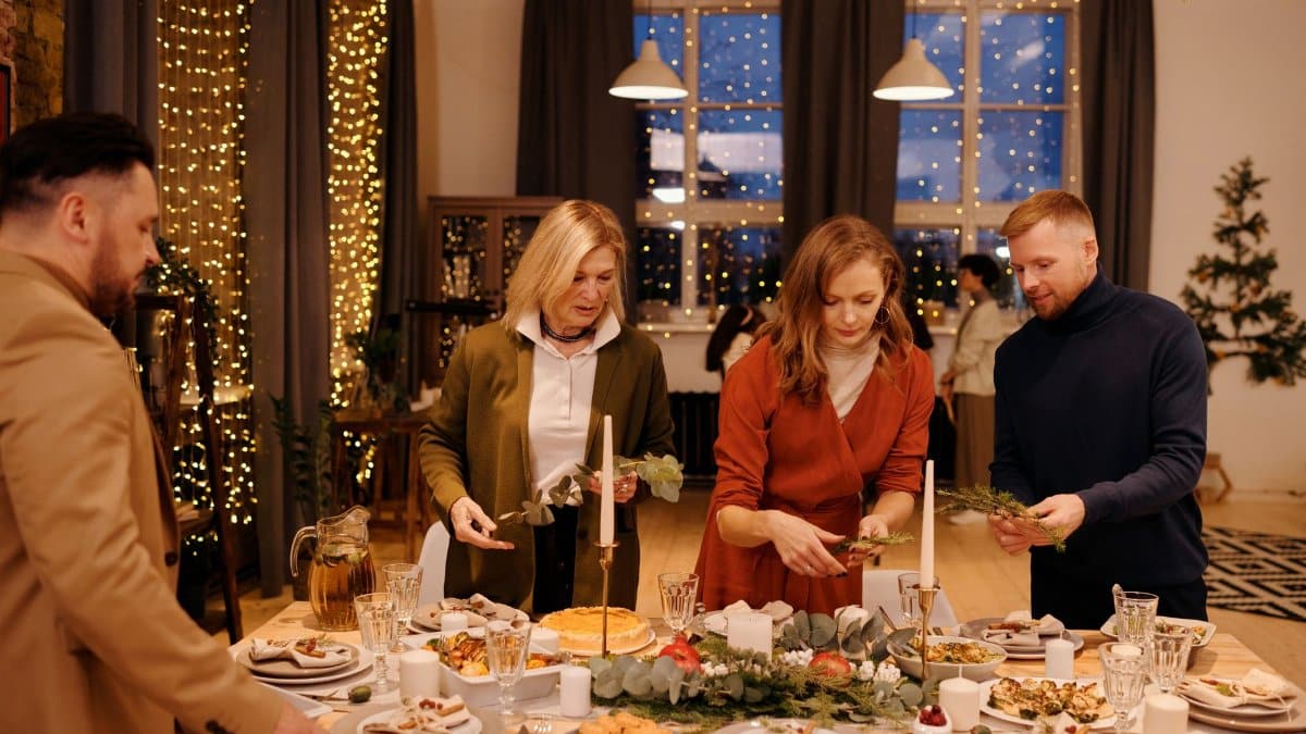 Family setting a festive table for Christmas dinner in a cozy, decorated home.