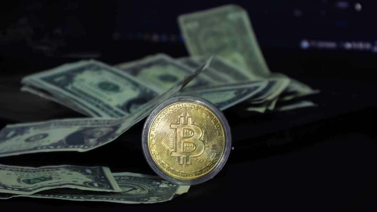 Bitcoin coin surrounded by scattered US dollar bills on a dark surface, symbolizing modern finance.