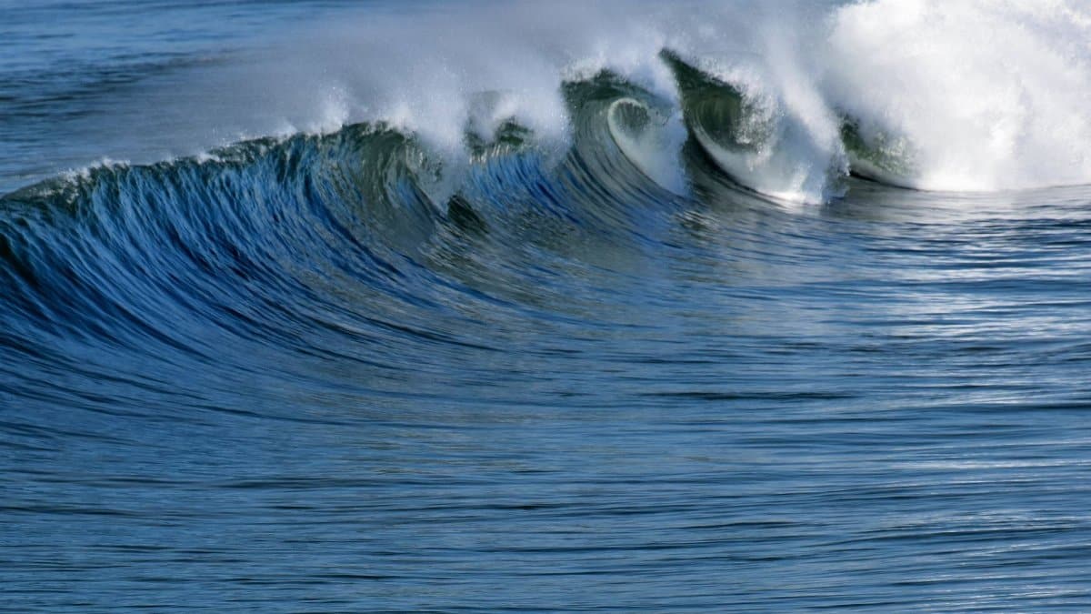Scenery view of blue rippled ocean with fast wave creating shiny splashes in daytime