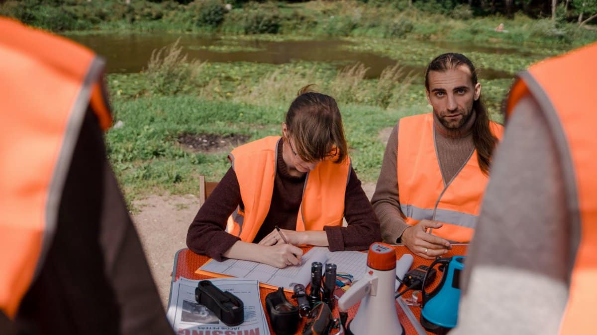 Volunteers in safety vests prepare for a search mission at a park near a water body.