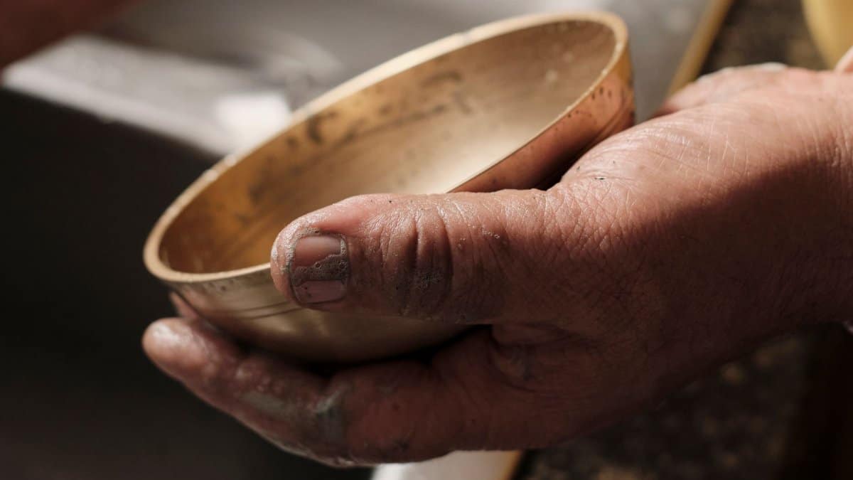 A detailed close-up of weathered hands holding an antique bronze bowl indoors.