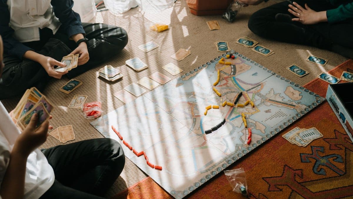 Kids enjoy a tabletop board game with map-based gameplay, cards, and tokens indoors.