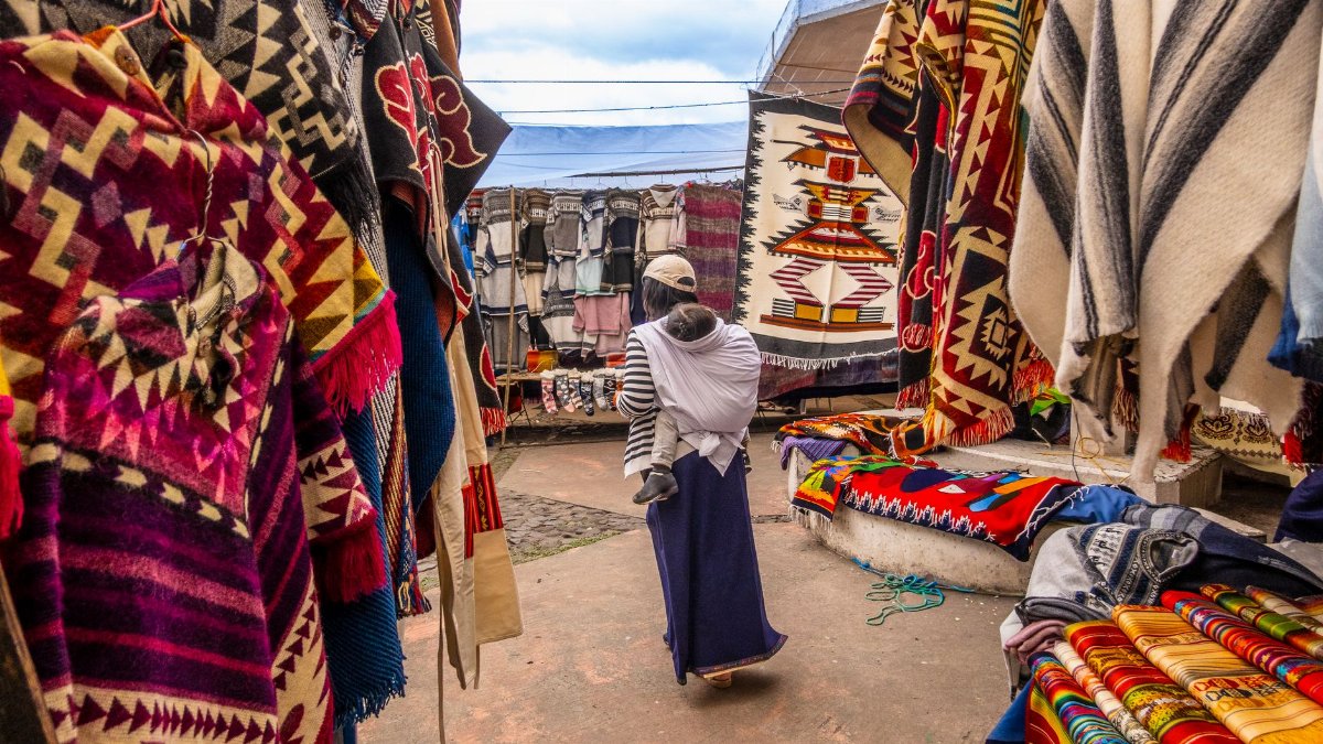 Colorful display of traditional textiles at a bustling outdoor market with a local shopper.