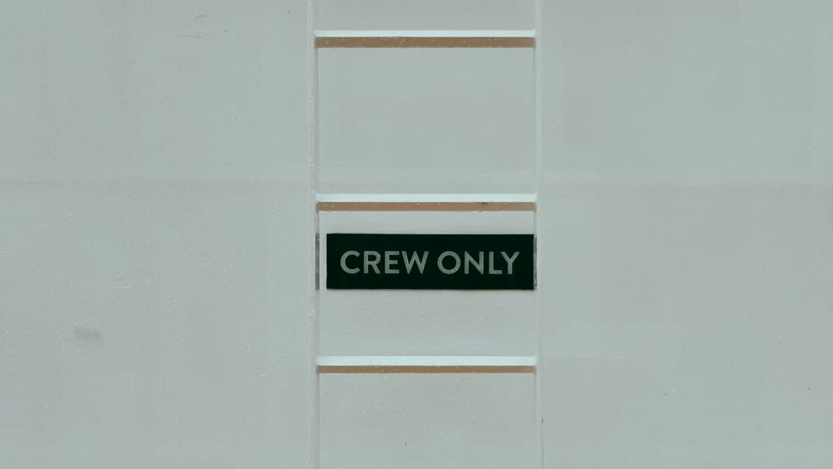 A minimalistic image featuring a 'Crew Only' sign on a ladder against a white wall.