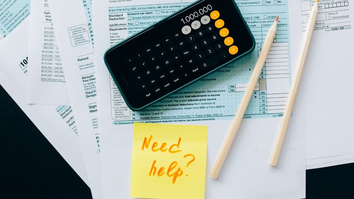 Top view of financial papers with a calculator, pencils, and a note saying 'Need help?' indicating tax or accounting assistance.